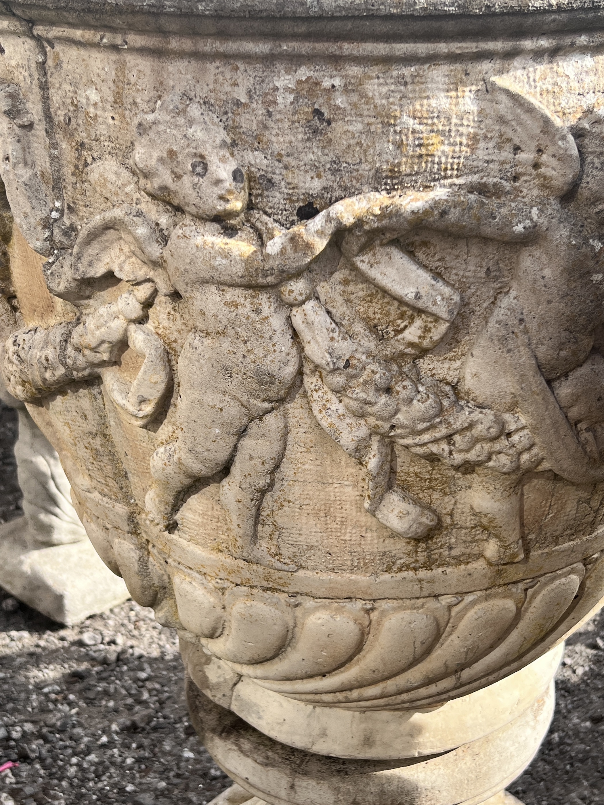 A pair of large circular reconstituted stone garden planters, moulded with a band of putti on square bases, diameter 53cm, height 89cm